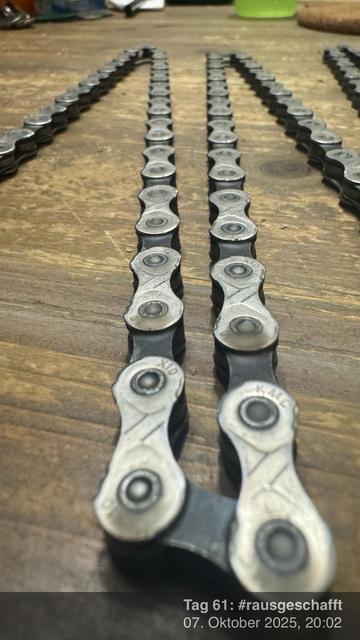Ein Nahaufnahmebild einer Fahrradkette, die auf einer Holzoberfläche ausgelegt ist, wobei die metallischen Glieder und Verbinder der Kette sichtbar sind.