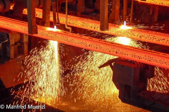 Orange glühendes Metall mit Funkensprühen in einer Stranggießanlage im Stahlwerk