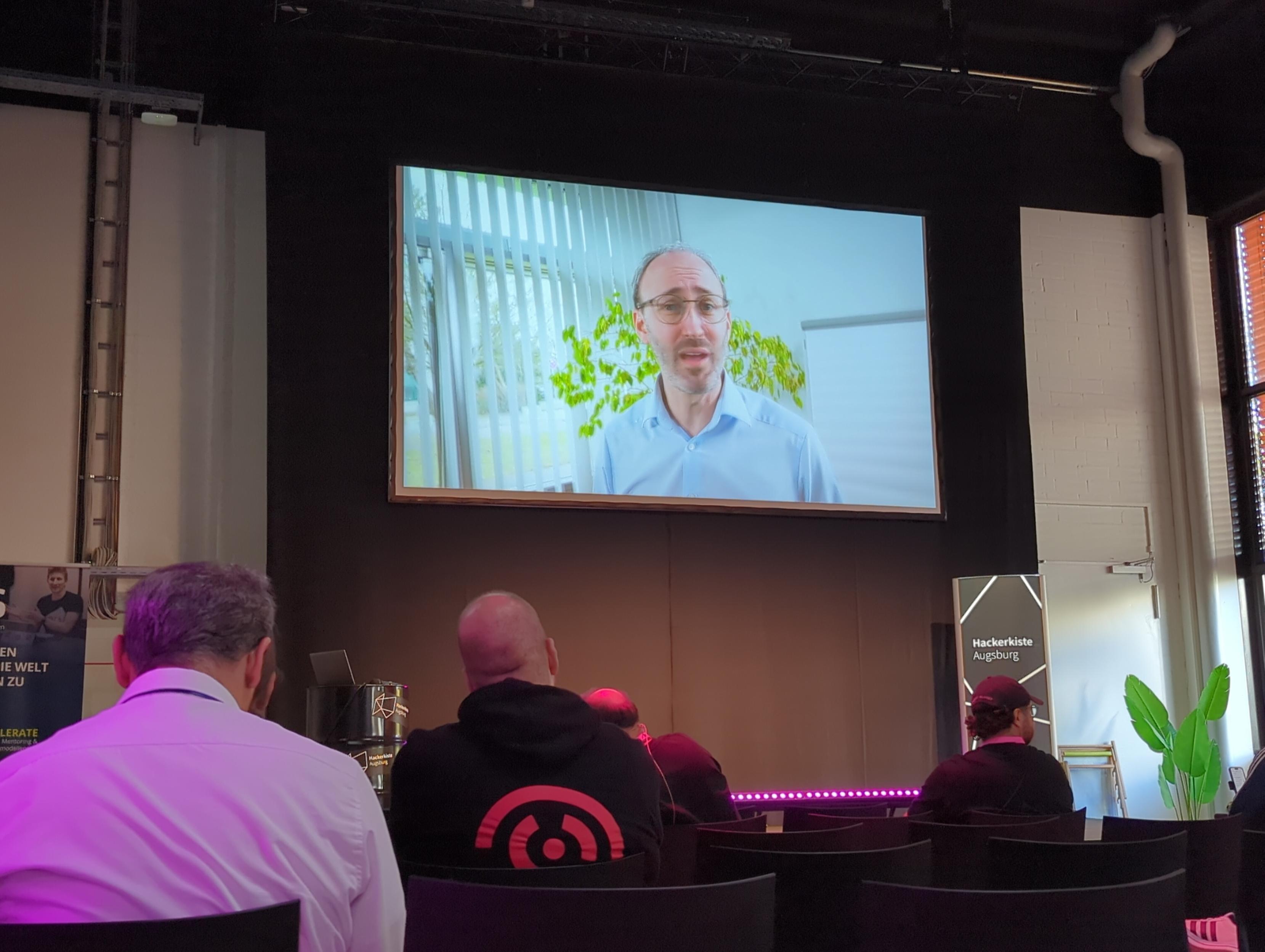 Video Ausschnitt aus dem Musikvideo auf der Leinwand. Im Vordergrund Zuschauer