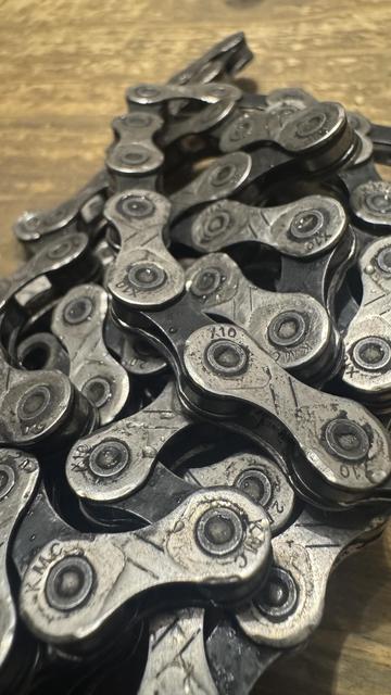 Ein Nahaufnahmebild eines Haufens von metallischen Fahrradkettengliedern, die ihre unterschiedlichen Formen und Texturen auf einer Holzoberfläche zeigen.