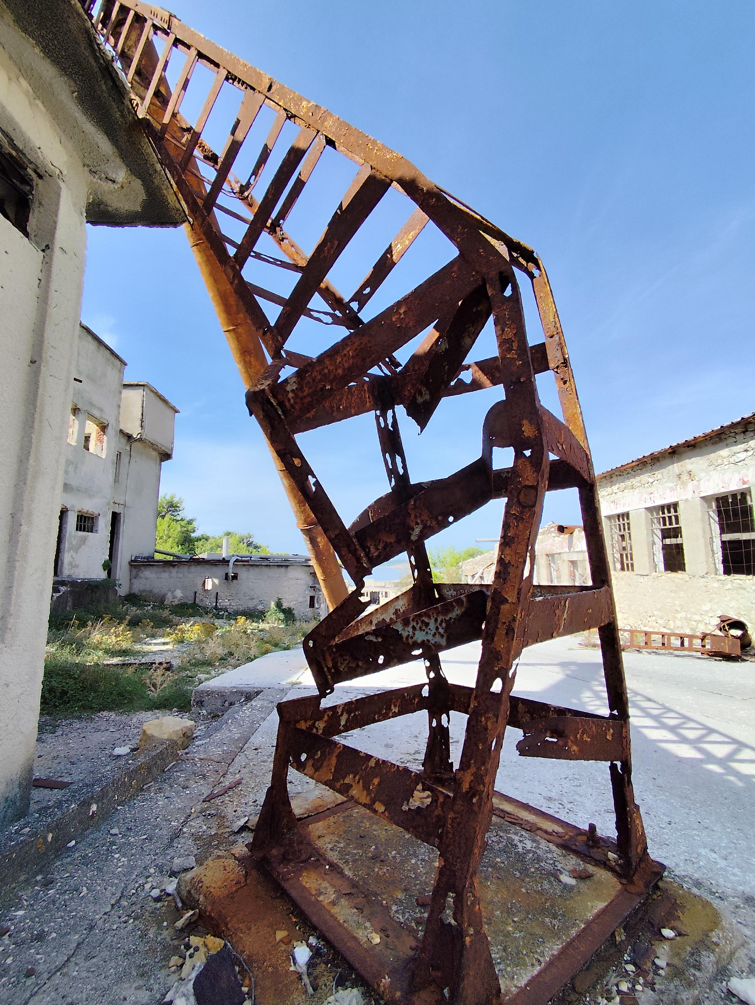 Abgeknickter, rostiger, alter 'Gitter' Mast zwischen Baracken