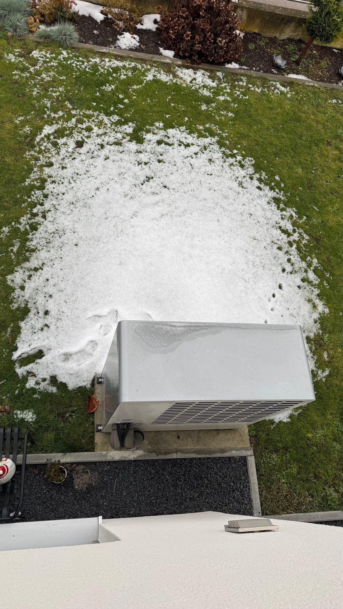 Wärmepumpe, vor der noch ein bisschen Schnee liegt. Weiter weg liegt kein Schnee mehr.